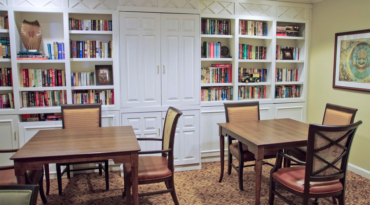 A cozy library room with bookshelves, tables, and chairs for reading.