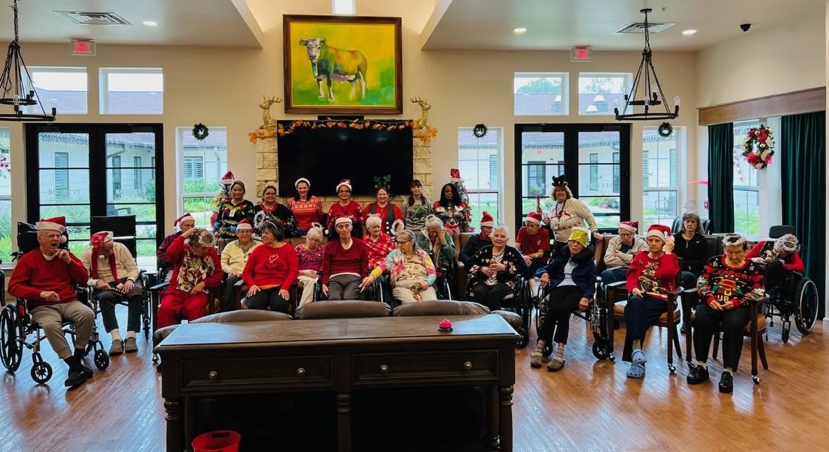 A group of people dressed in festive clothing gather for a Christmas celebration inside a decorated room.