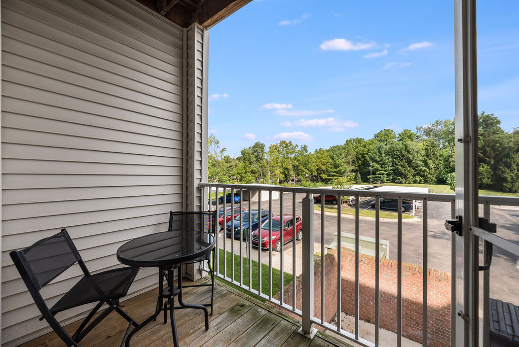 A view from a balcony with seating overlooking a parking lot and trees under a clear blue sky.
