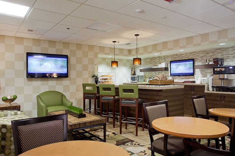 A modern lounge area featuring a bar with seating, multiple television screens, and comfortable chairs.
