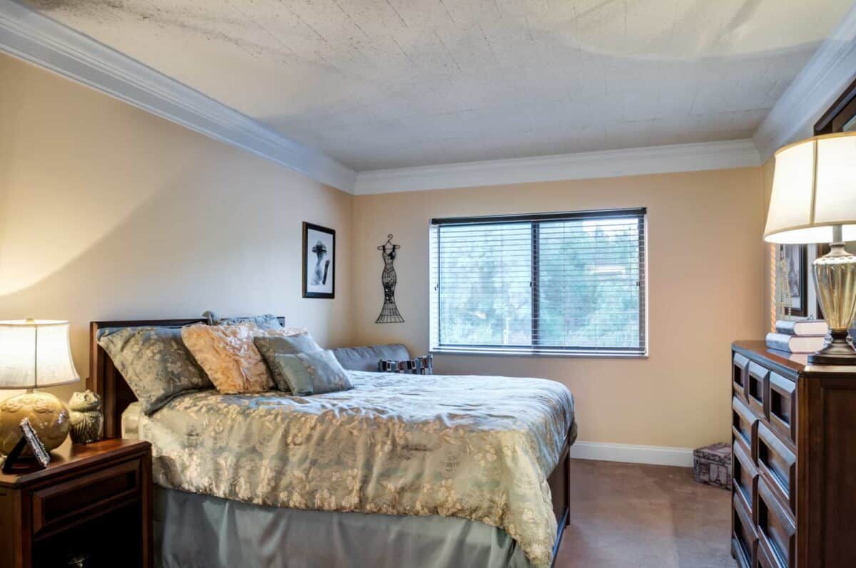 A cozy bedroom interior with a neatly made bed and large window.