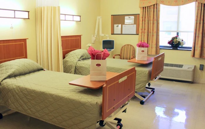 A clean and well-organized hospital patient room with two beds and flowers on the tables.