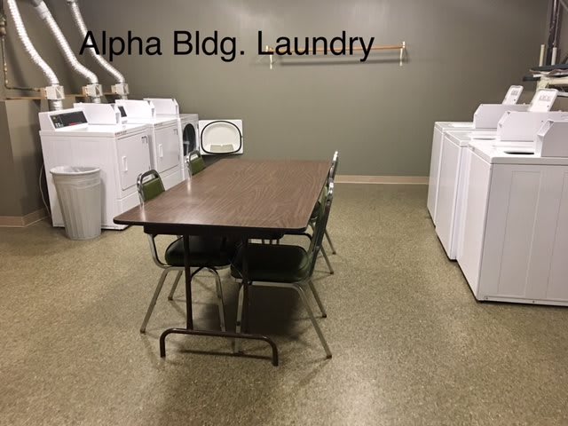 A laundry room with washing machines, dryers, and a table with chairs.