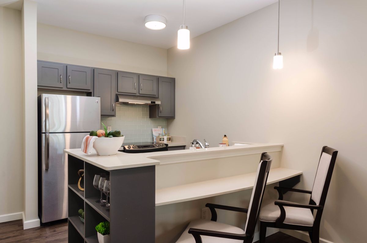 A modern kitchen with stainless steel appliances and a small dining area with bar stools.
