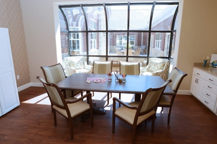 A well-lit conference room with a large table and six chairs arranged around it, set against a backdrop of large windows.
