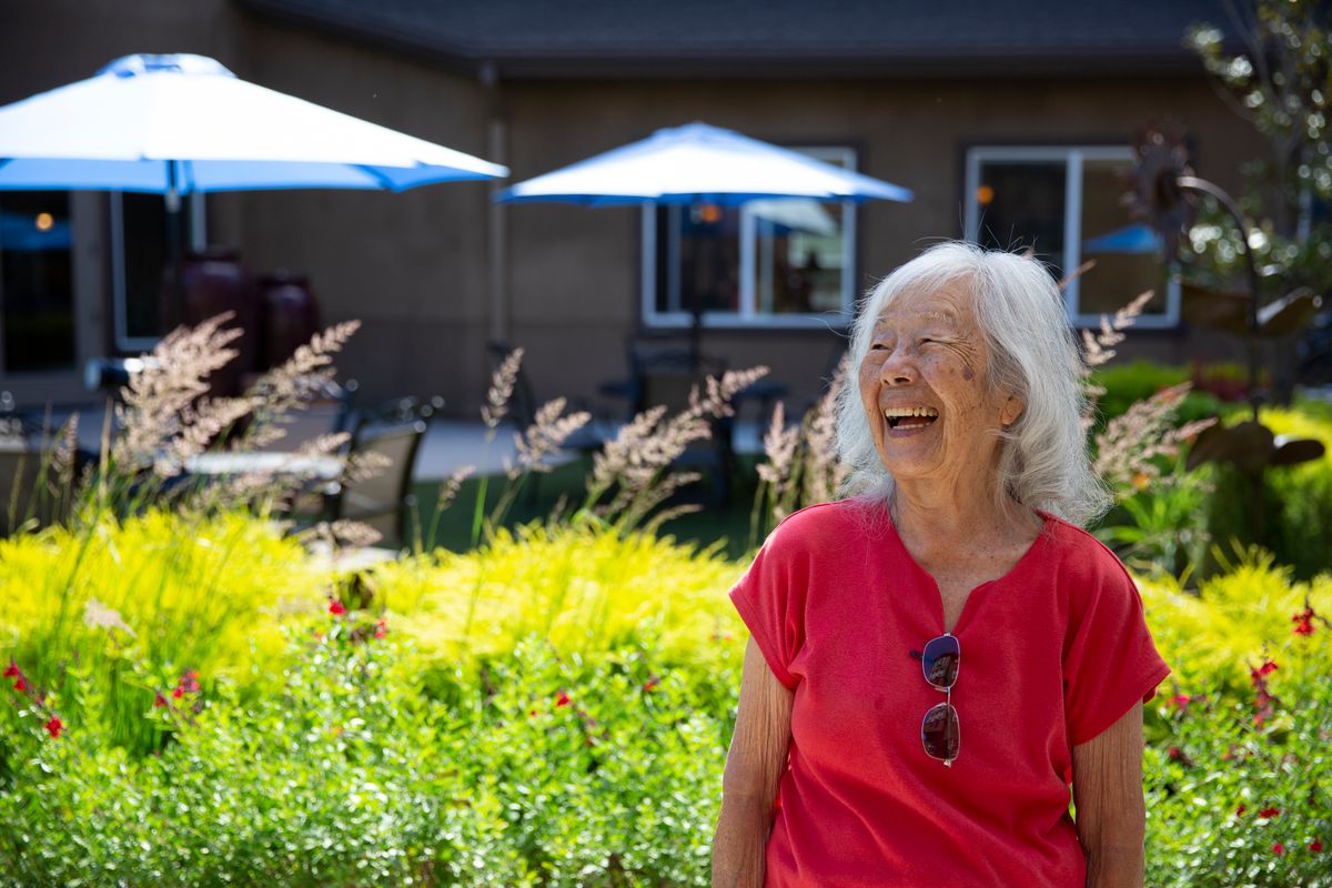An elderly woman enjoys a sunny day in a garden, smiling brightly.