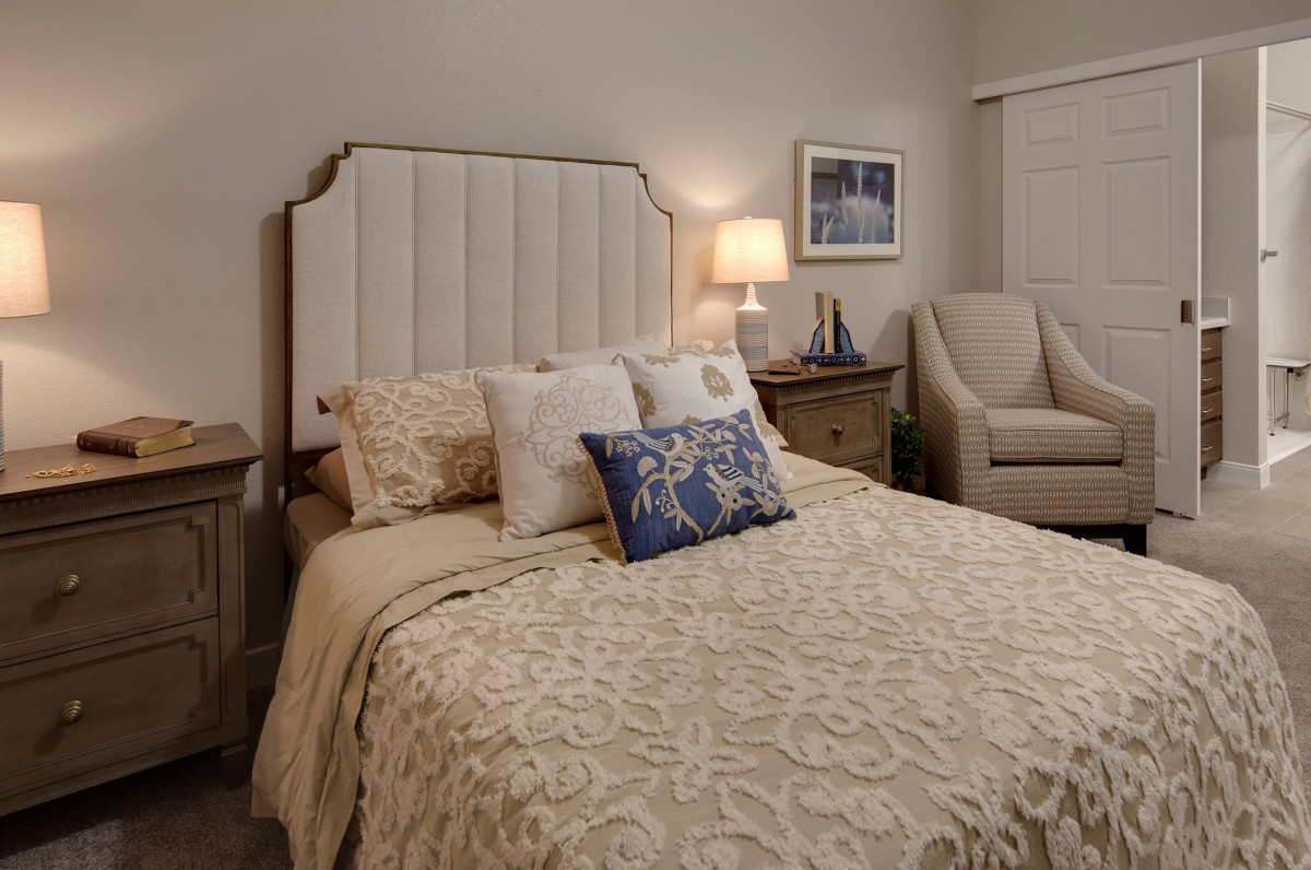 A cozy bedroom with a neatly made bed, upholstered headboard, and warm lighting.
