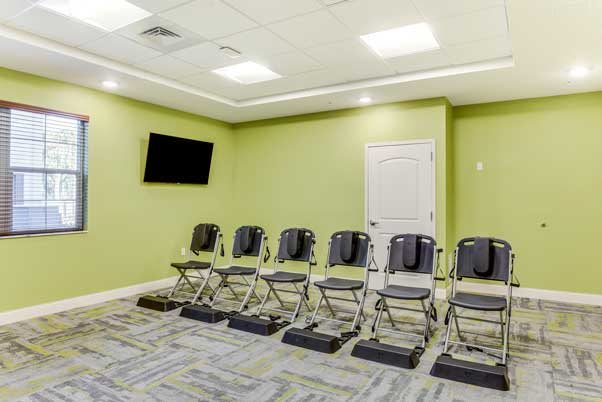 An empty waiting room with green walls, featuring a row of chairs and a wall-mounted television.