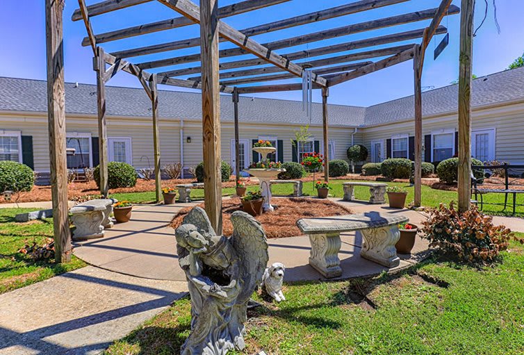 A serene courtyard with a pergola, stone benches, and decorative sculptures.