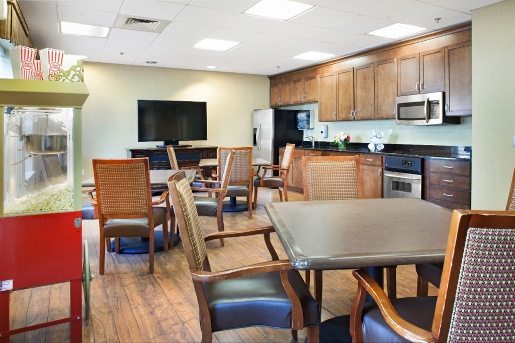 A modern dining and kitchen space featuring a television, multiple tables and chairs, wooden flooring, and built-in cabinets.
