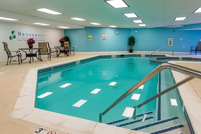 An indoor swimming pool with a handrail, blue walls, and seating area.