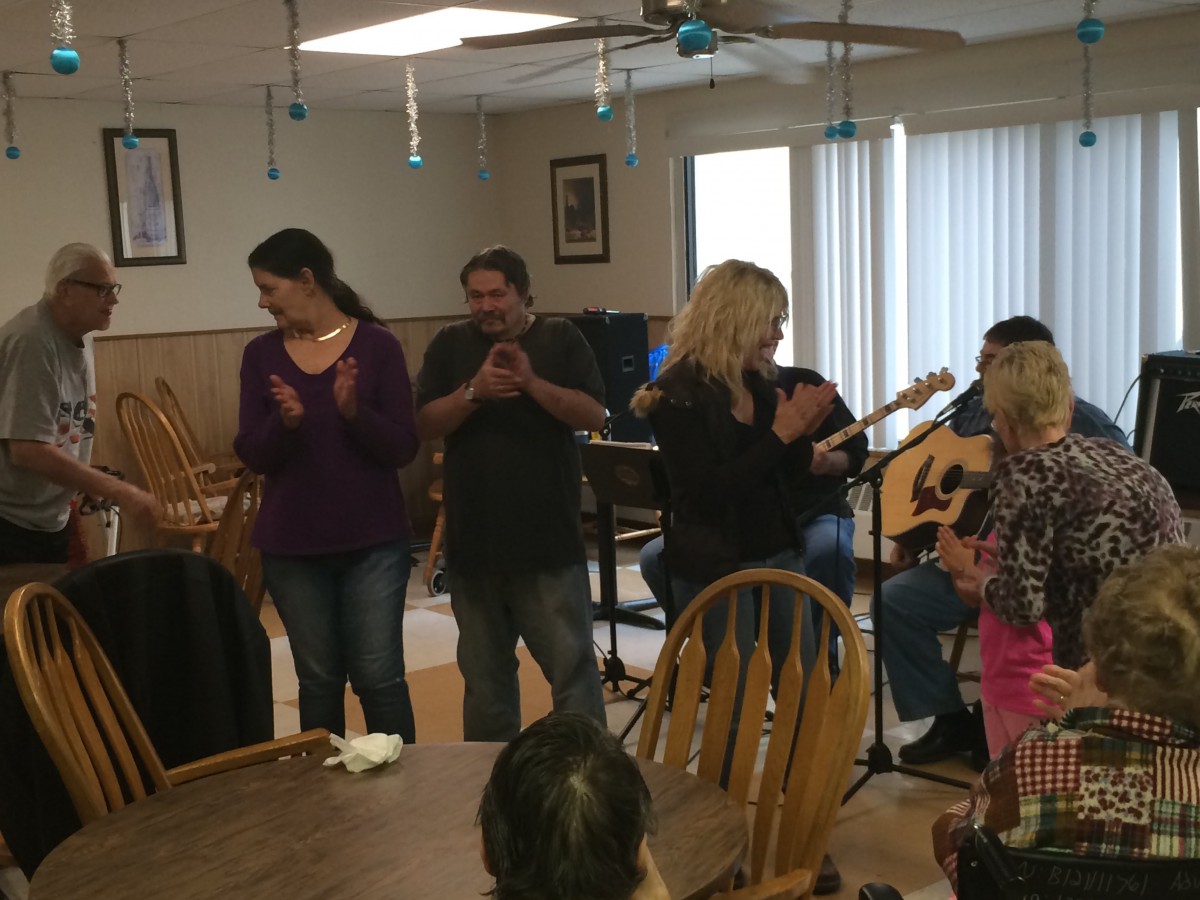 A group of people gathered indoors, clapping and celebrating.