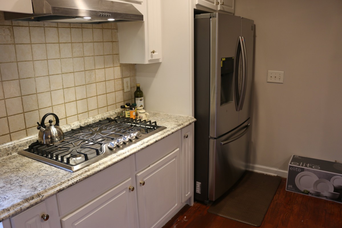 A modern kitchen area with a gas stove, refrigerator, and white cabinets.