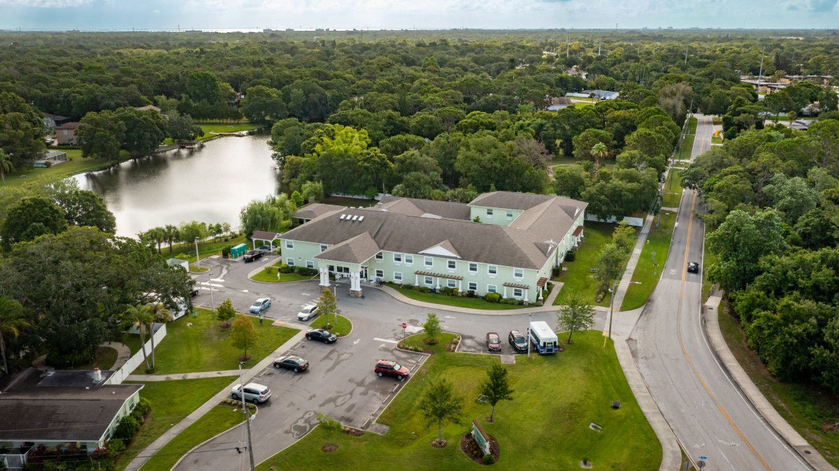 Aerial view of a residential building surrounded by trees and a nearby lake.