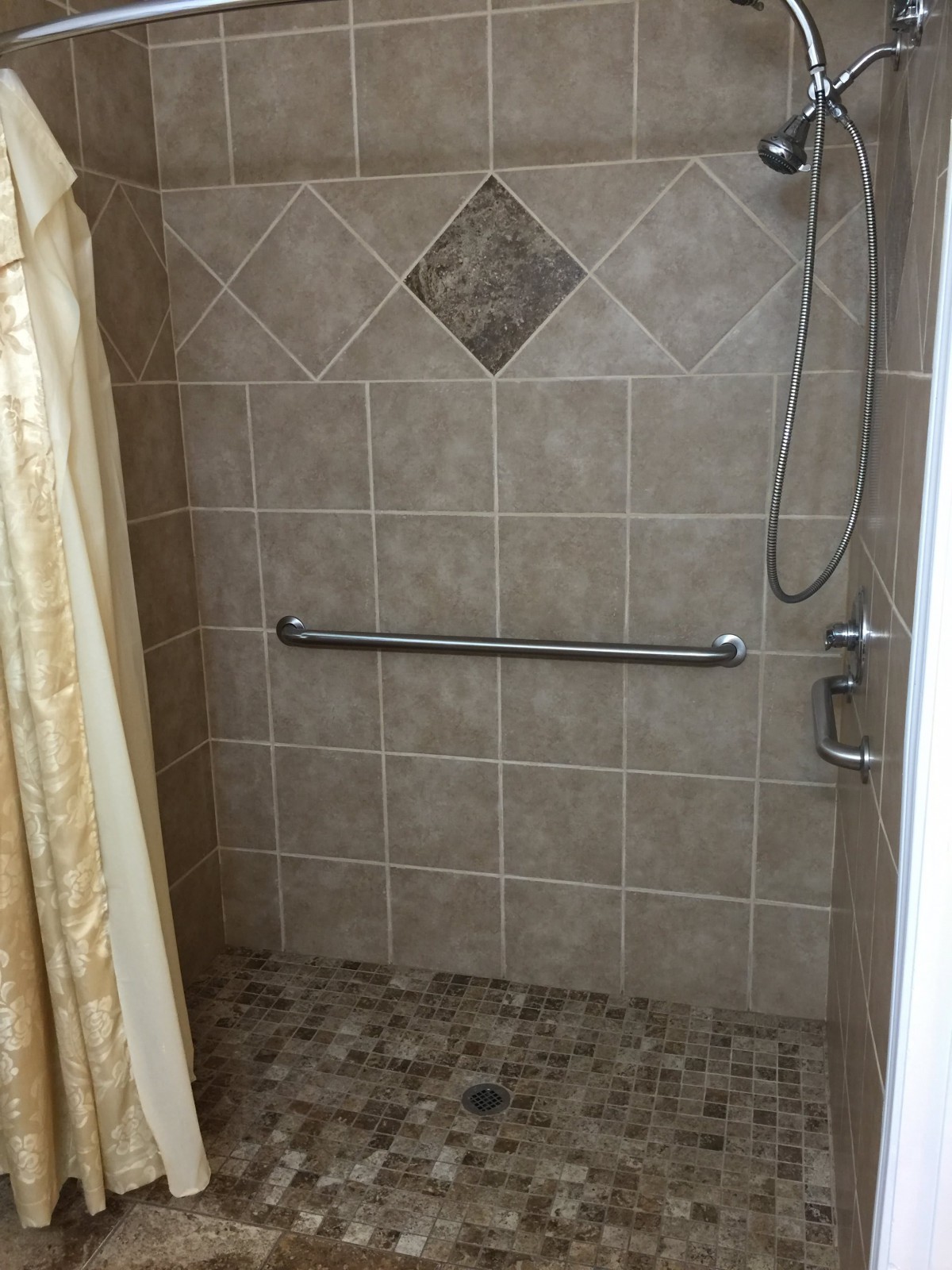 A tiled shower with a handrail and showerhead.