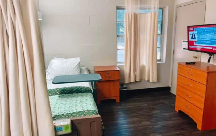 A simple hospital room with a bed, bedside table, and window with curtains.