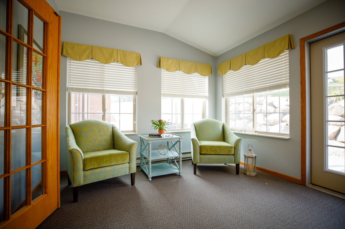 A cozy living room corner with two green chairs and large windows letting in natural light.