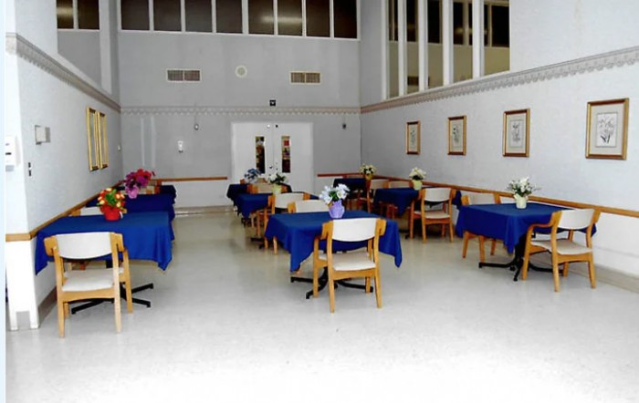 An indoor dining area with several tables covered in blue tablecloths and surrounded by chairs.