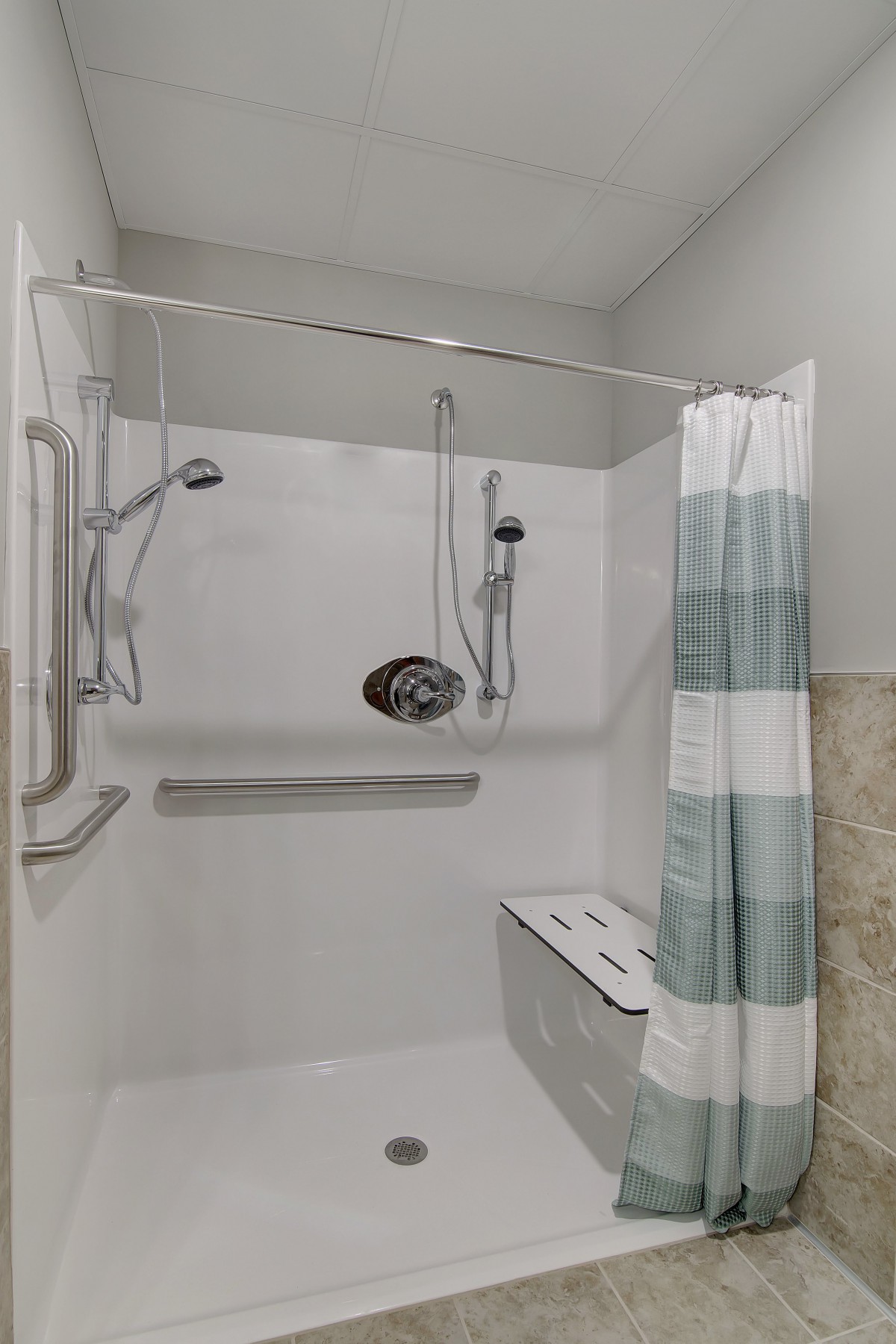Accessible bathroom with a shower area featuring grab bars, a handheld showerhead, and a bench seat.