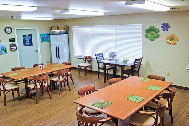 A cozy dining room with wooden tables and chairs, featuring large windows and bright lighting.