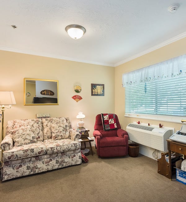 Cozy living room with a floral sofa, red armchair, and various decor under soft lighting.
