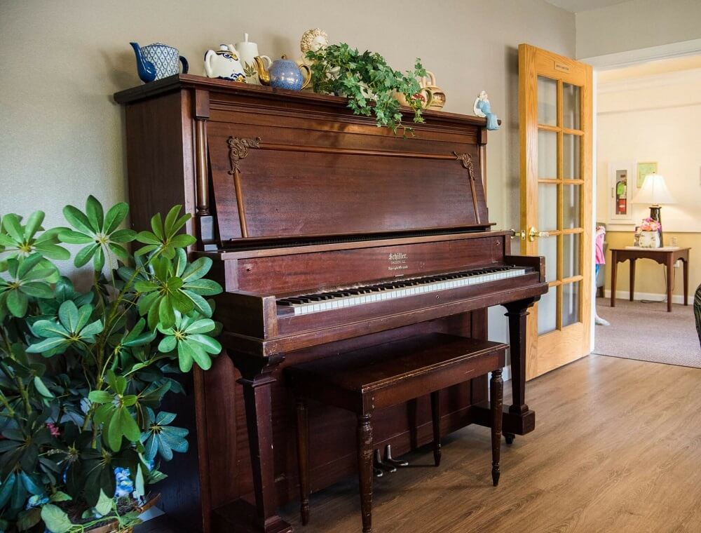 A wooden upright piano decorated with plants and ornaments in a cozy room.
