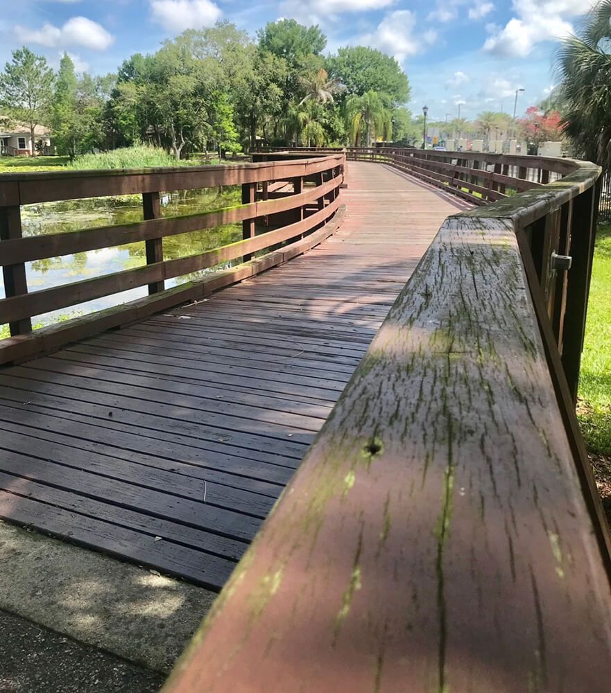 A wooden bridge curves over a serene landscape under a bright blue sky.