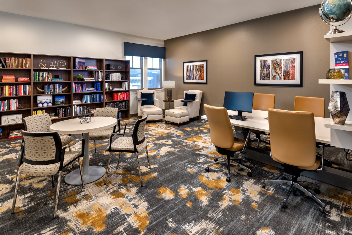 A modern office workspace featuring desks with computers, a bookshelf, and comfortable seating.
