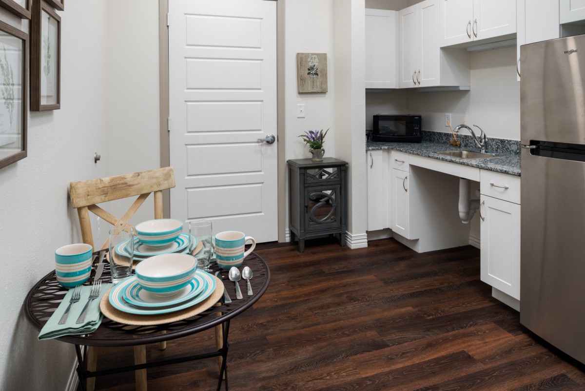 A modern kitchen with white cabinets and a neatly set dining table on a dark wooden floor.