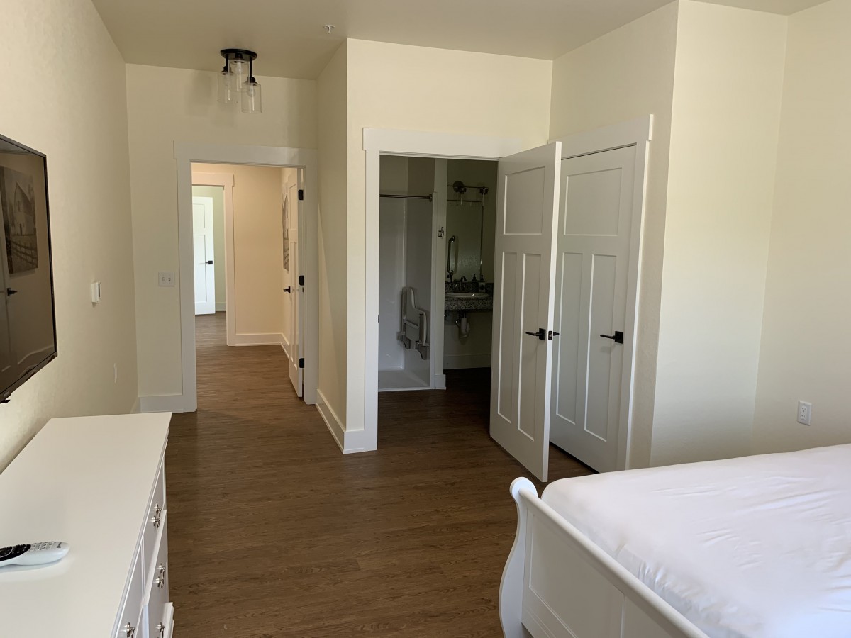 A tidy bedroom with wooden flooring, featuring a bed and a closet.