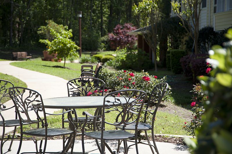 A serene garden setting featuring metal patio furniture surrounded by lush greenery and vibrant flowers.