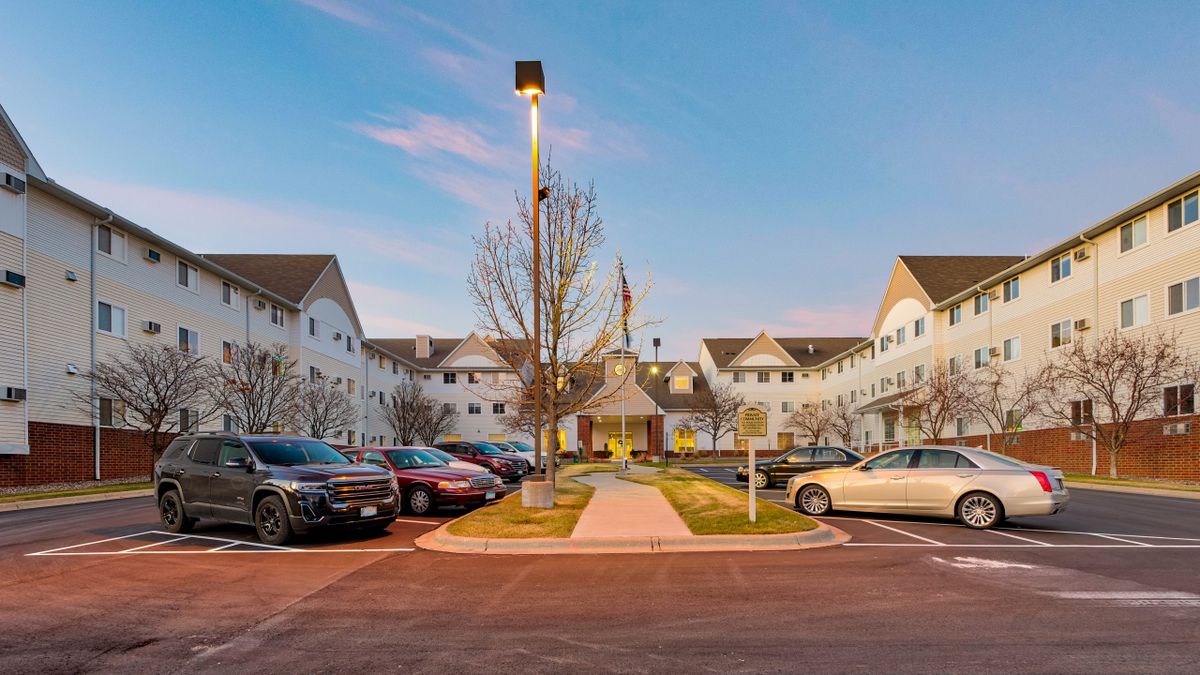 A residential building with a parking lot and cars at sunset.