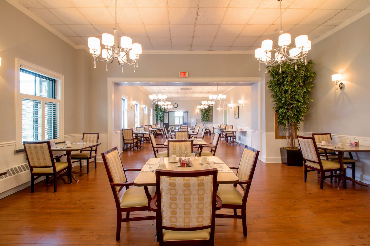 Elegant dining area with neatly arranged tables and chairs, illuminated by decorative chandeliers.