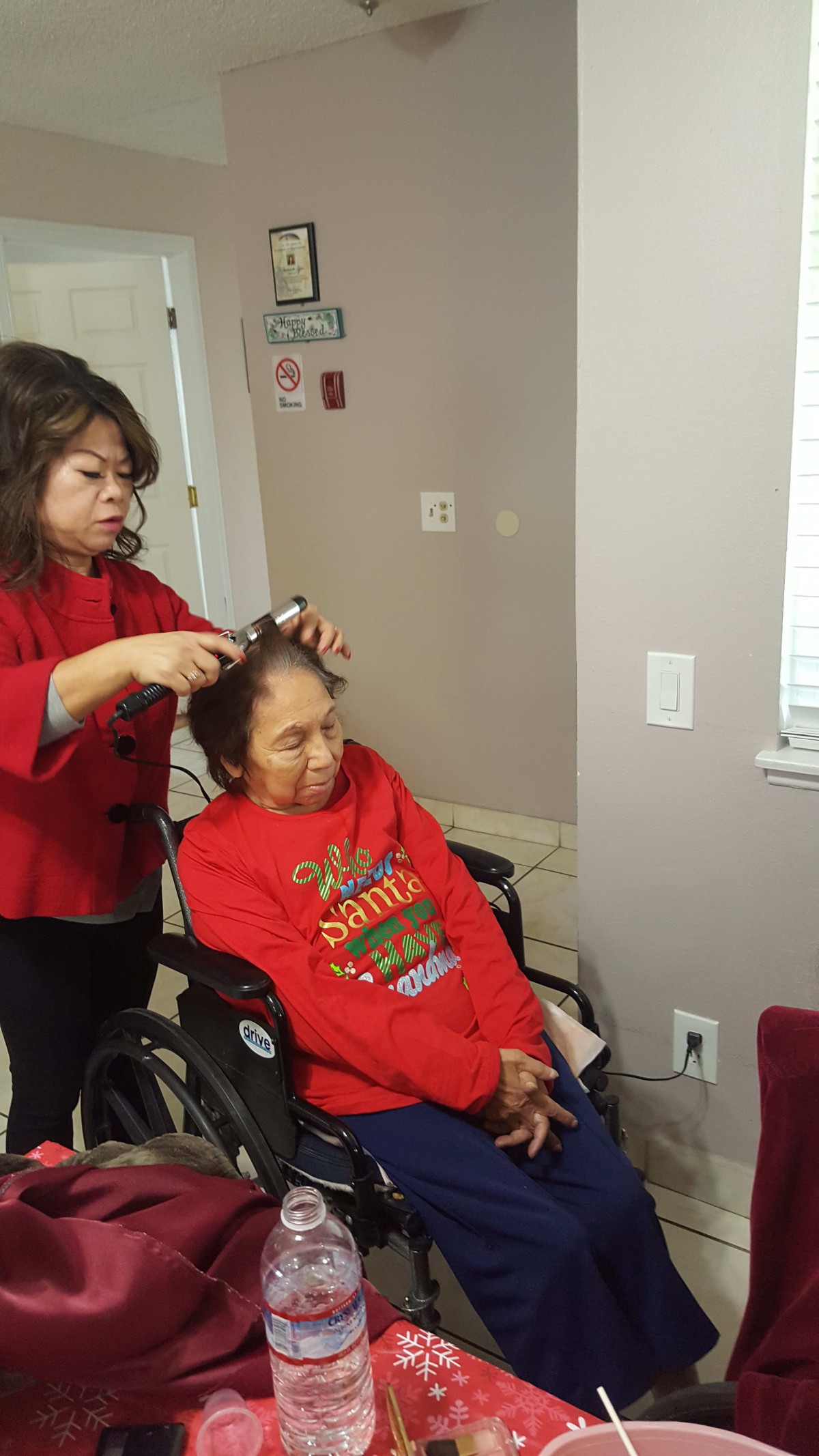 A caregiver styles the hair of a person seated in a wheelchair.
