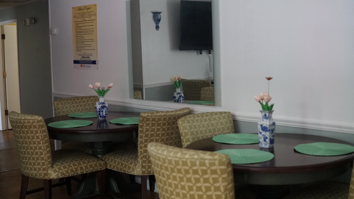 A cozy dining area with round tables, upholstered chairs, and flower vases reflecting in a mirror.