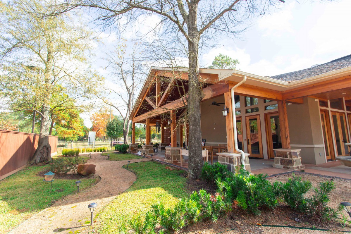 A wooden building with large windows surrounded by trees and a landscaped garden on a sunny day.