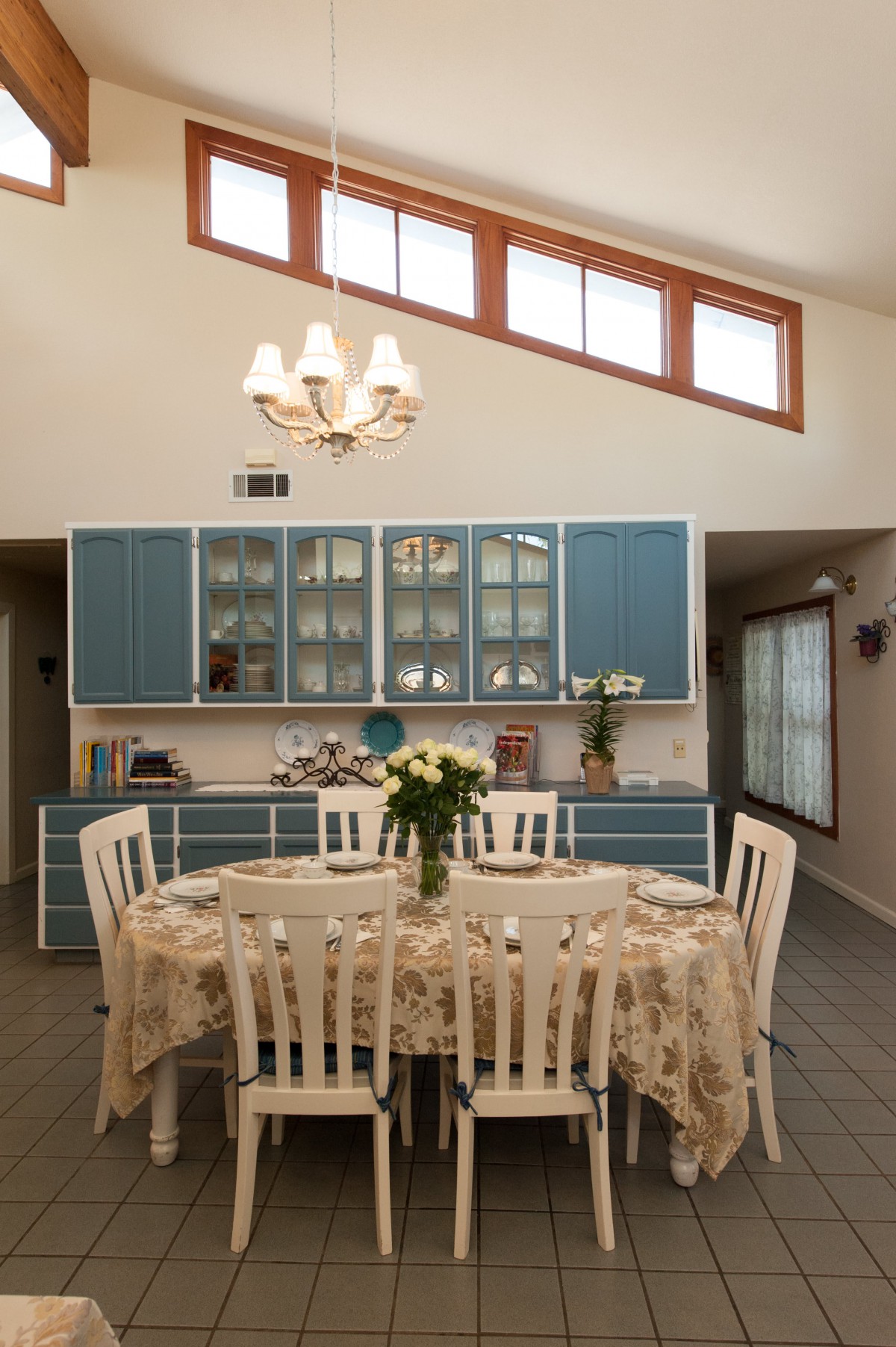 A cozy kitchen with a round dining table, adorned with flowers and surrounded by blue cabinetry.