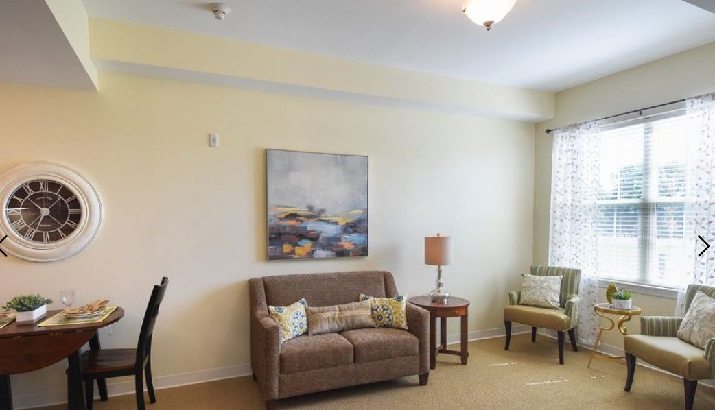 A cozy living room featuring a sofa with cushions, a side table with a lamp, and a painting on the wall.