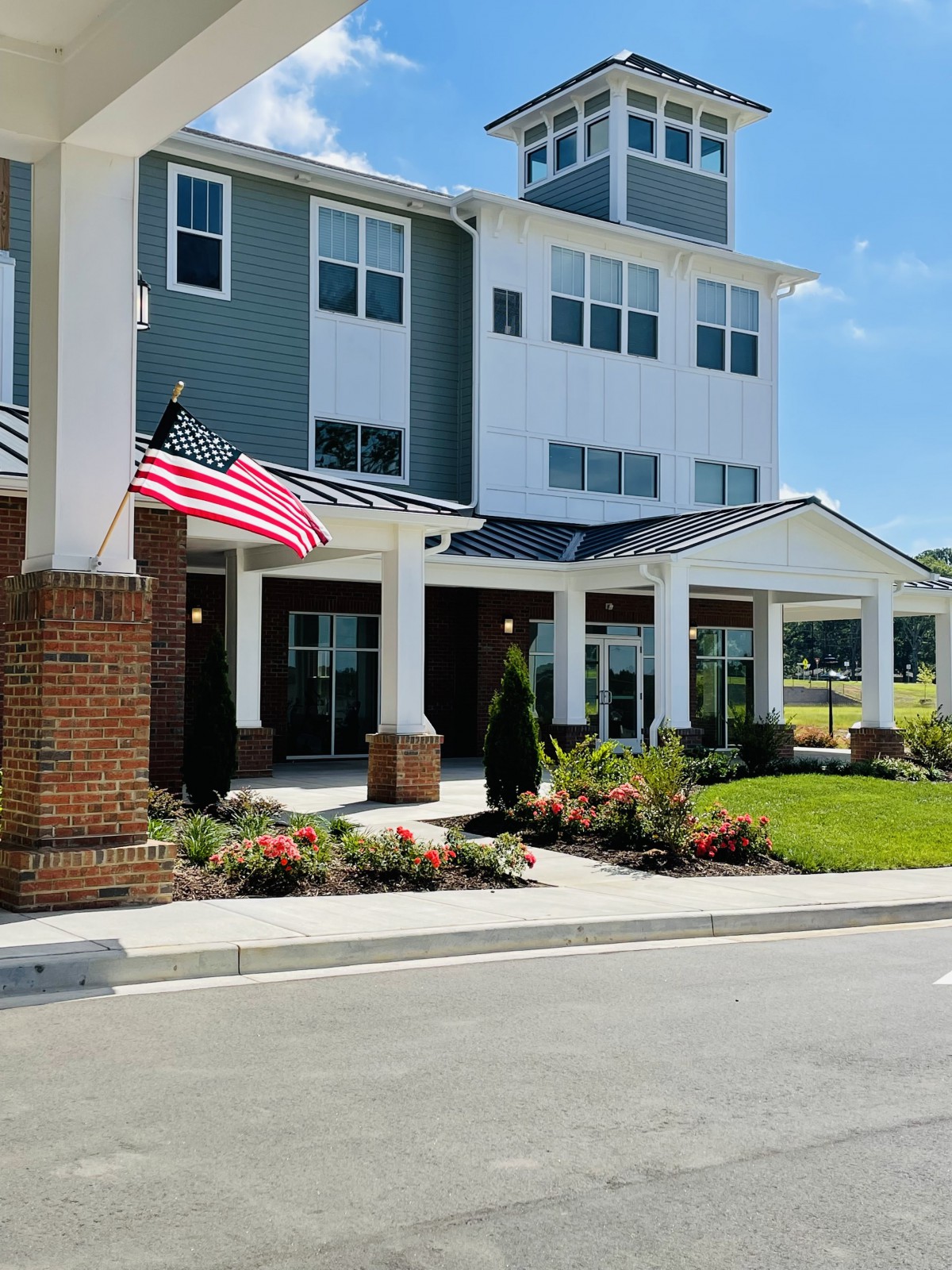 A residential building entrance with landscaping and an American flag on a sunny day.