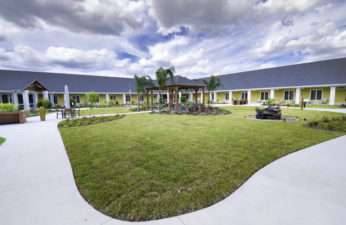 A scenic view of a courtyard garden with well-maintained lawns surrounded by a modern building and a cloudy sky above.