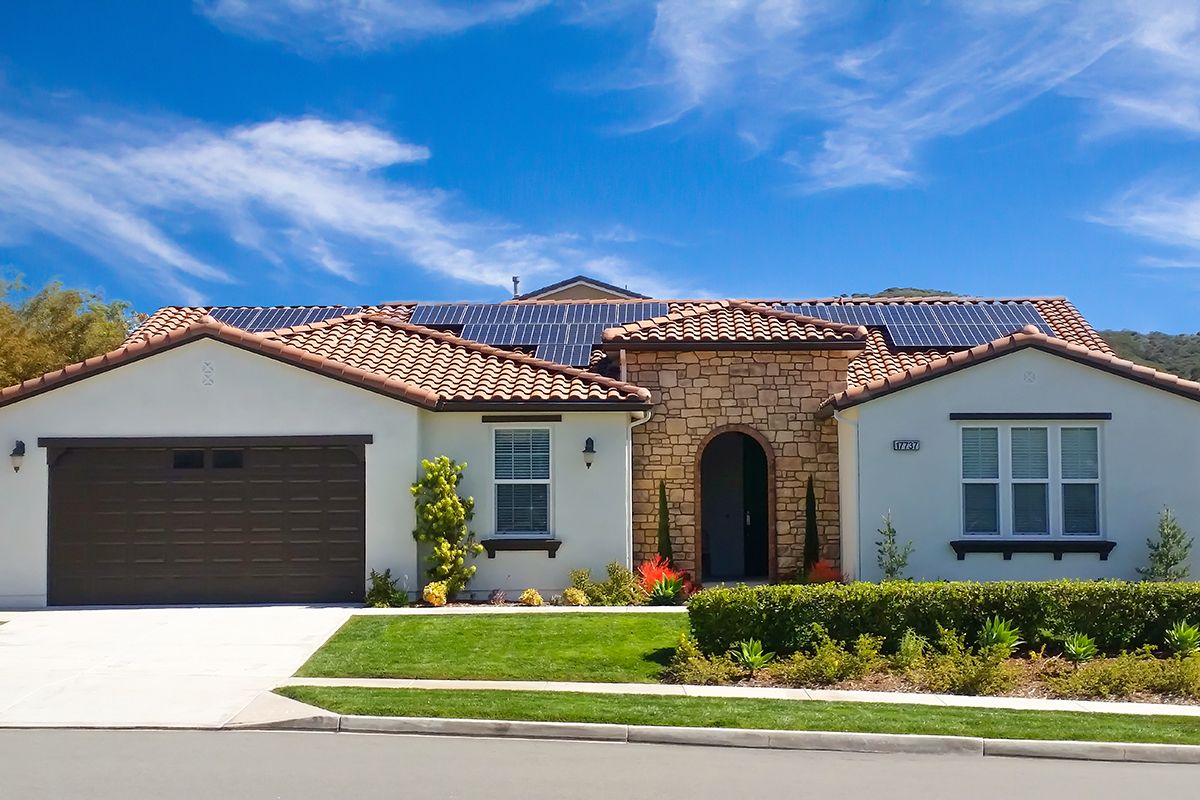 A modern house with solar panels on the roof, a well-maintained garden, and a driveway.
