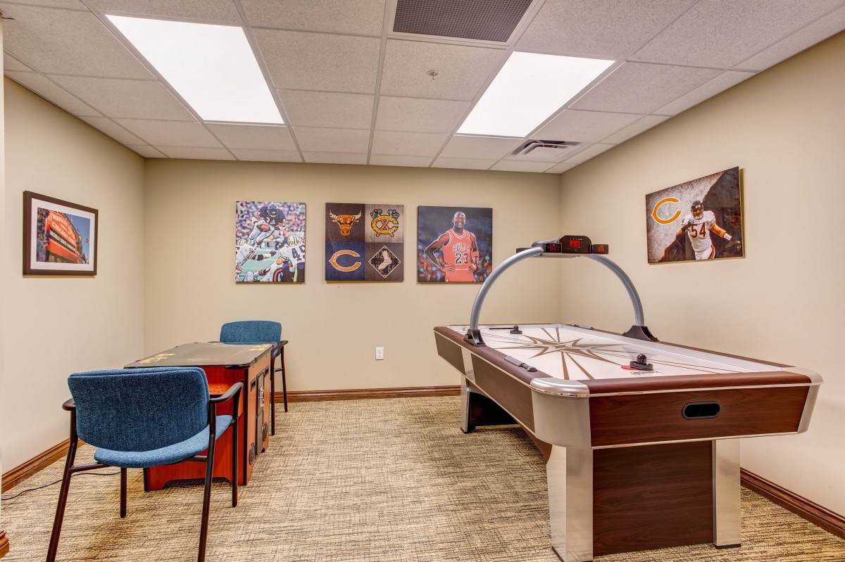 A game room featuring an air hockey table, a small table with chairs, and colorful posters on the walls.
