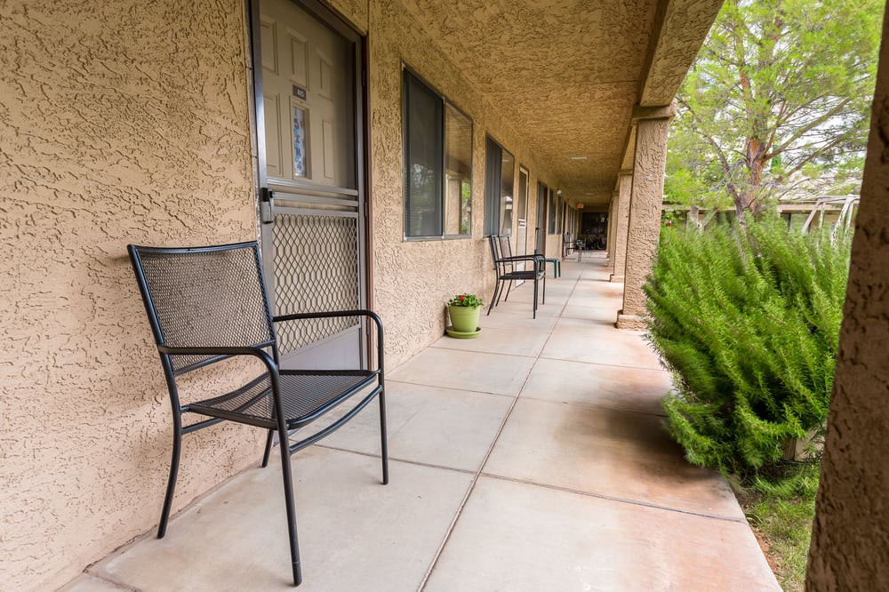 A view of a motel corridor with metal chairs and potted plants along the walkway.