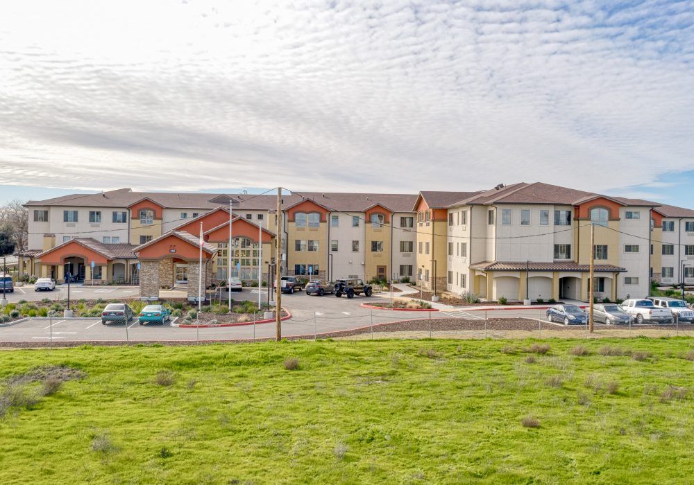 A modern apartment complex with a spacious parking lot, set against a cloudy sky.
