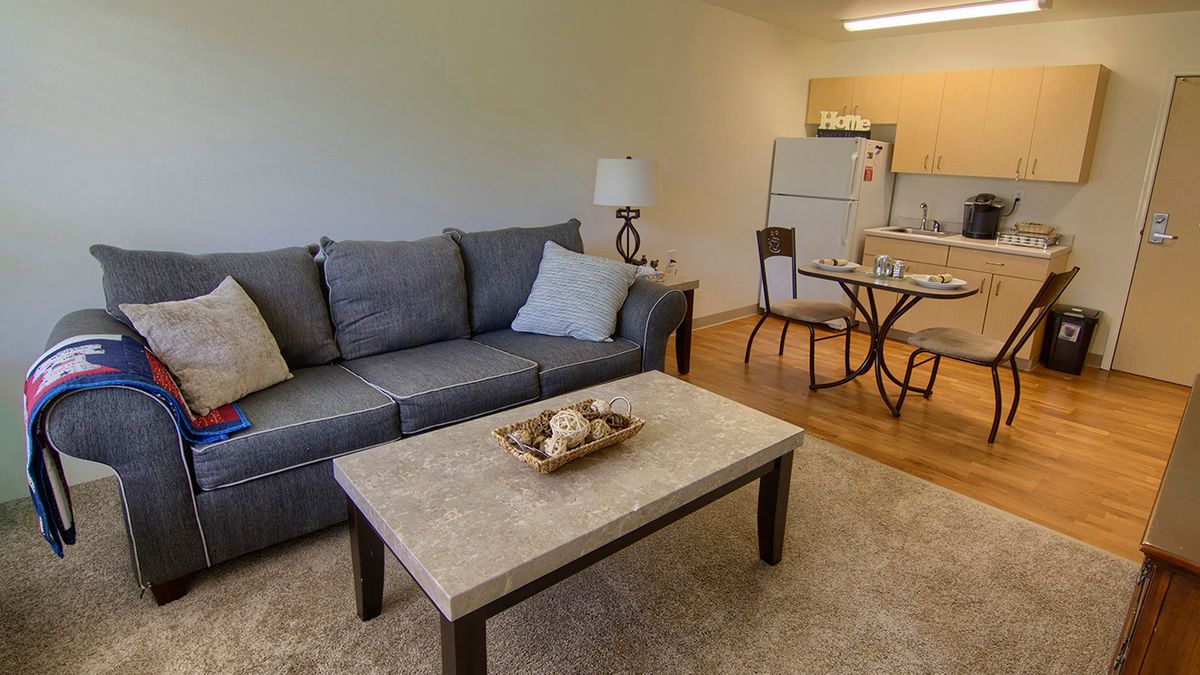A cozy apartment living space featuring a comfortable sofa, coffee table, and an adjoining dining area with a kitchen in the background.