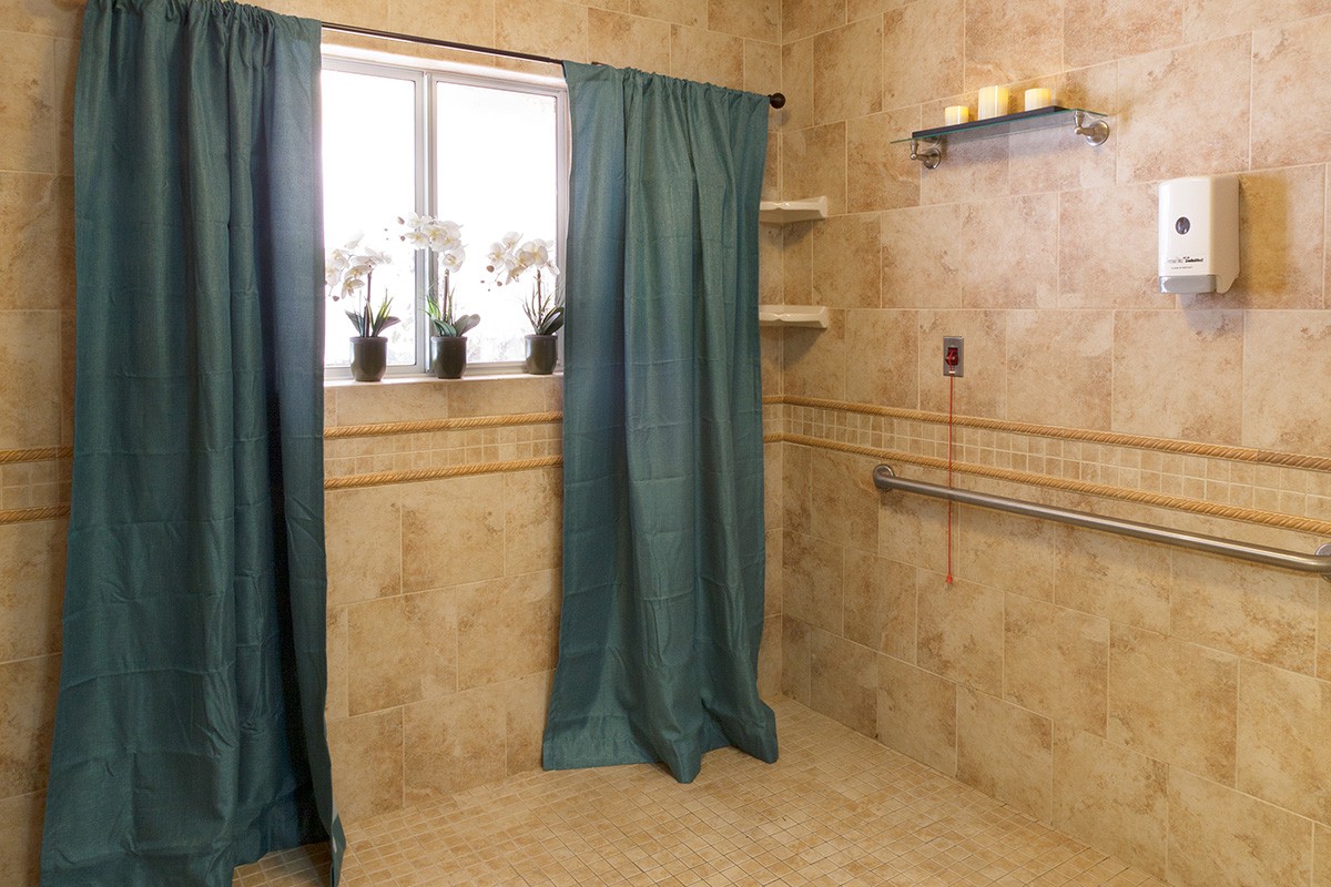 A tiled bathroom with a window, green curtains, and decorative elements like plants and candles.