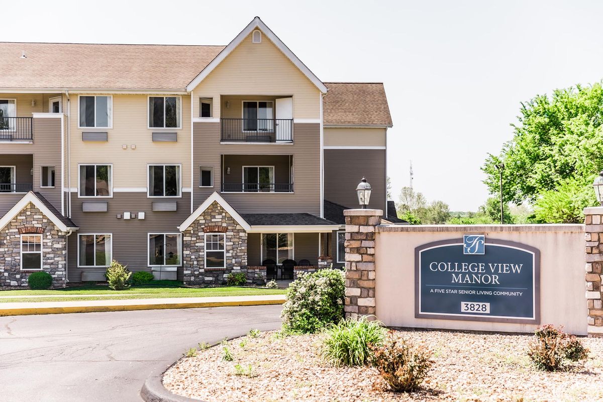 A modern apartment complex with a welcoming sign in the foreground, surrounded by neat landscaping.