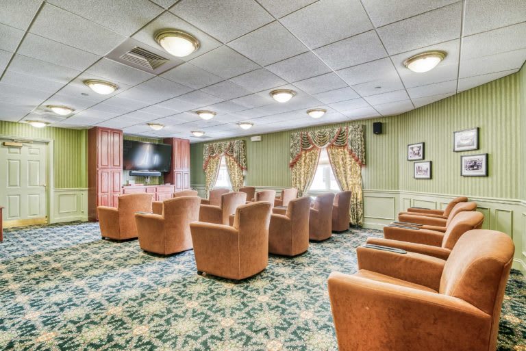 A small theater room with comfortable chairs and a large television, featuring elegant curtains and a patterned carpet.