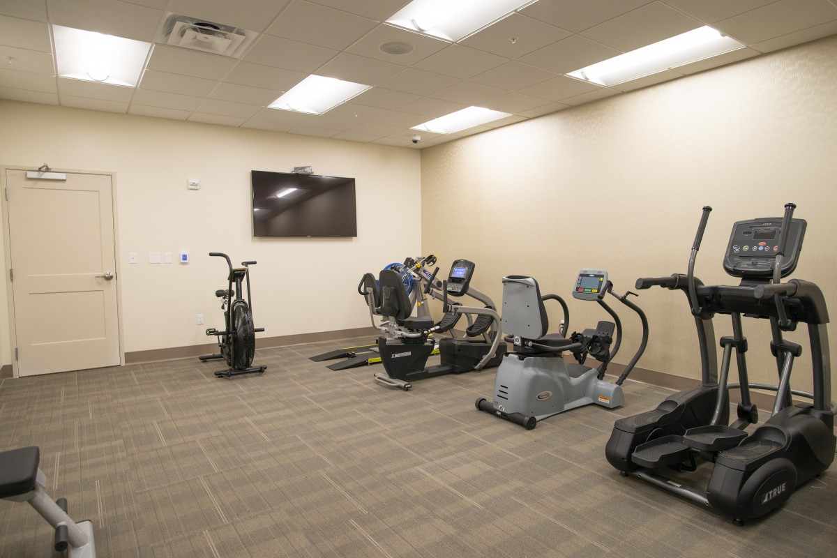 A small gym with various fitness equipment including a treadmill, stationary bike, and elliptical machine.