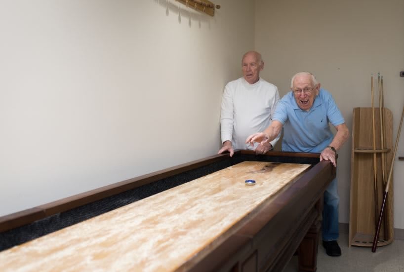 Two elderly men playing shuffleboard indoors.